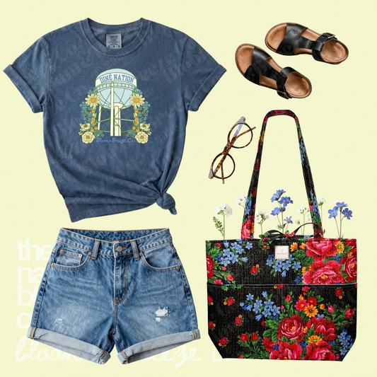Blue Diné Nation water tower graphic tee styled with denim shorts, black sandals, glasses, and a black floral quilted tote bag.