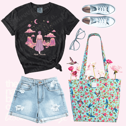 Black t-shirt with graphic design, denim shorts, floral tote bag, and sneakers on a pink background