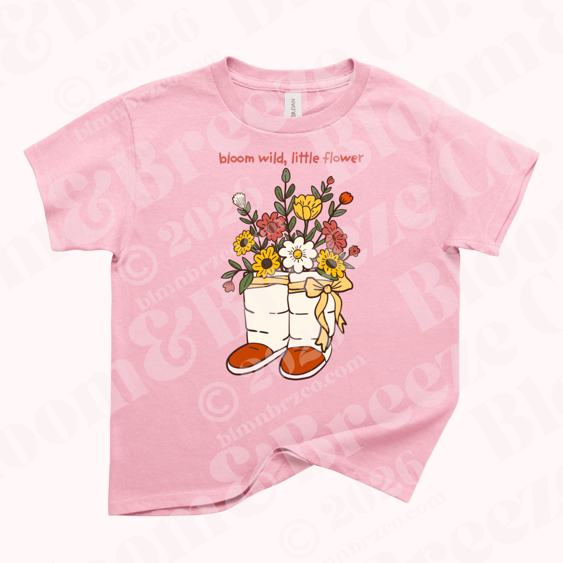 Pink youth t-shirt with illustration of Navajo wrap moccasins filled with colorful wildflowers and the words “bloom wild, little flower” above the design.