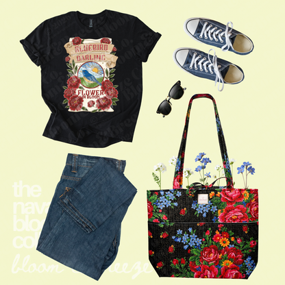Black Bluebird Darling graphic tee styled with dark jeans, navy sneakers, sunglasses, and a black floral quilted tote bag.