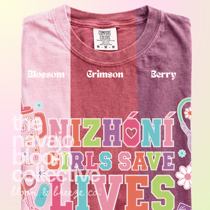 Nizhóní Girls Save Lives colorful lettering and medical-themed artwork on a Comfort Colors tee, comparing Blossom, Crimson, and Berry.