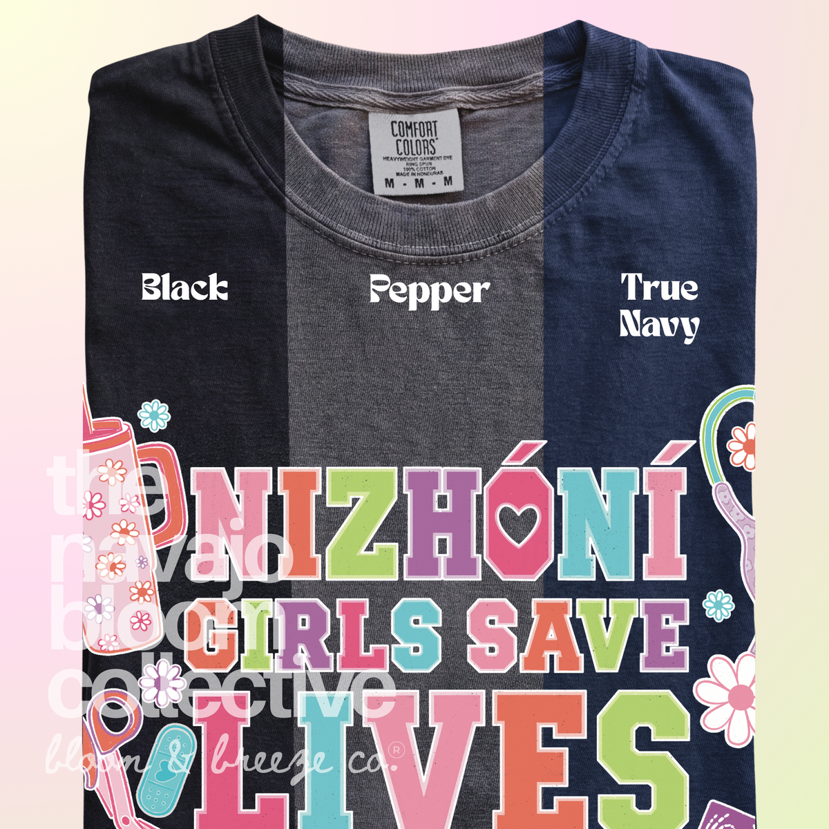 Nizhóní Girls Save Lives colorful lettering and medical-themed artwork on a Comfort Colors tee, comparing Black, Pepper, and True Navy.