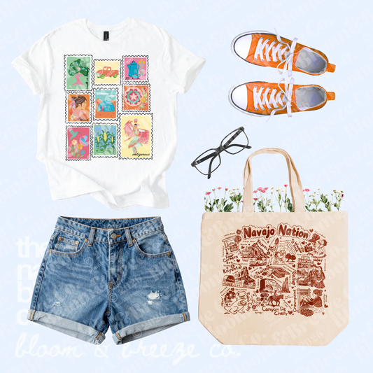 White Navajo stamp graphic tee styled with denim shorts, orange sneakers, black glasses, and a Navajo Nation tote bag.