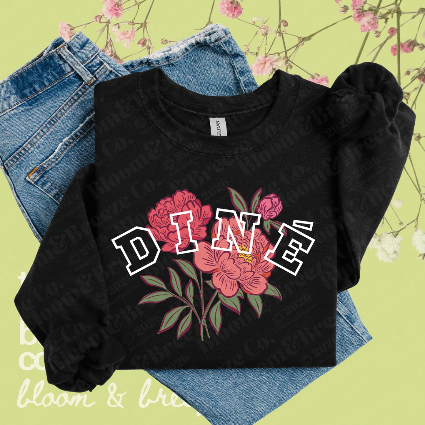 Black Diné floral sweatshirt layered over denim jeans on a soft green floral background.