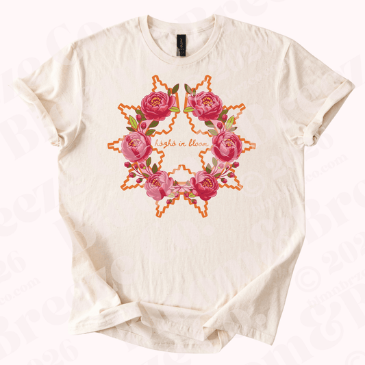 Beige t-shirt with Navajo wedding basket inspired design with peonies and text “Hozho in bloom” on a white background