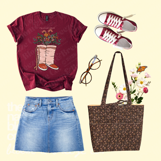 Maroon wildflower moccasin graphic tee styled with a denim skirt, red sneakers, glasses, and a brown floral quilted tote bag.