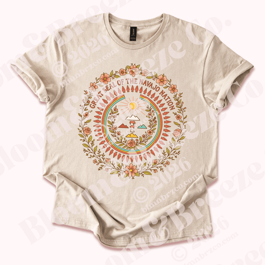Beige t-shirt with nation in bloom design, navajo nation seal with a boarder of pink flowers around seal, on a white background