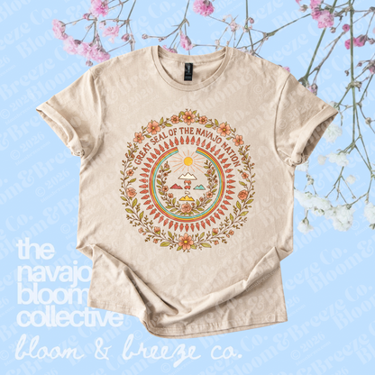 Cream Great Seal of the Navajo Nation graphic tee with floral details on a light blue floral background.