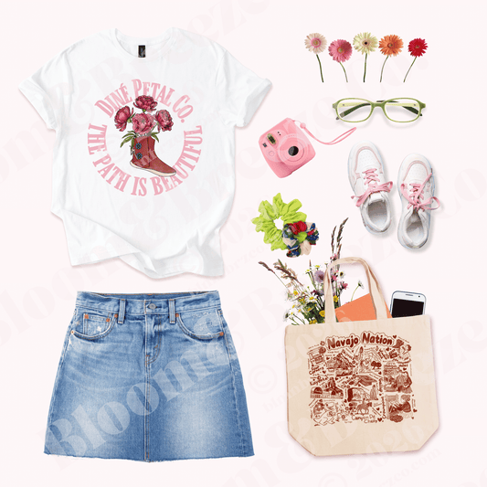 White graphic tee reading “Dinè Petal Co. The Path Is Beautiful” styled with denim skirt and a cream canvas tote featuring a Navajo Nation illustration filled with landmarks and cultural icons