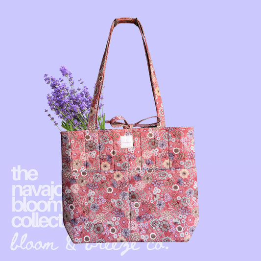 Coral floral quilted tote bag with long straps, front pockets, and lavender flowers on a soft purple background.