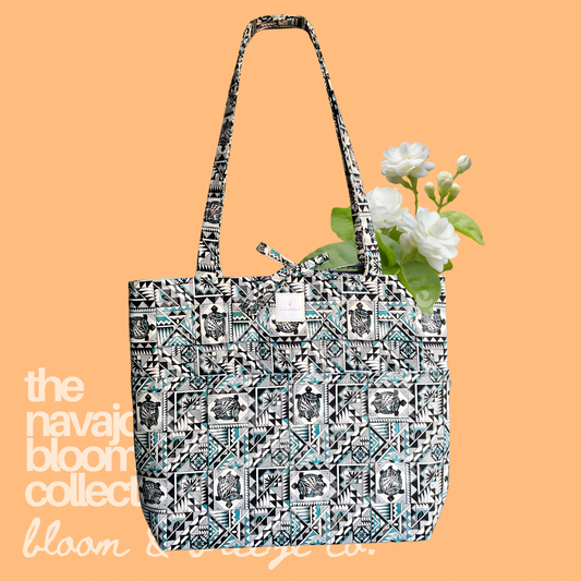 Black, white, and turquoise geometric quilted tote bag with long straps, front pockets, and white flowers on a soft orange background.