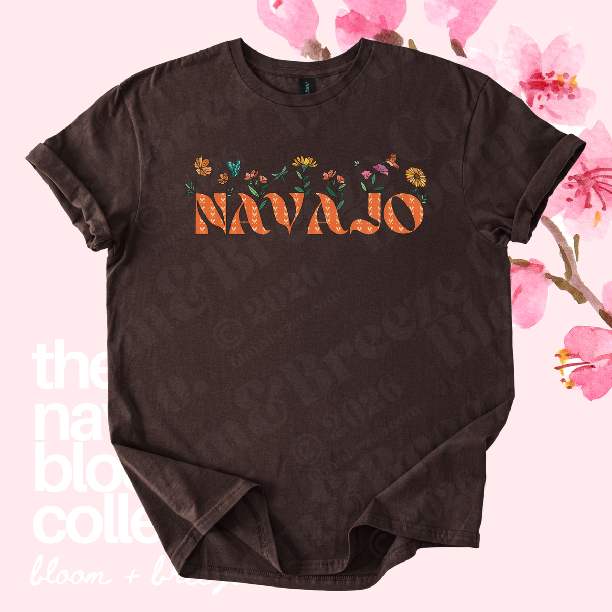 A dark brown short-sleeve t-shirt with a graphic on the chest featuring the word 'NAVajo' in orange letters filled with a floral pattern, surrounded by small multicolored flowers. The shirt is displayed flat against a light pink background decorated with cherry blossom graphics and faint text watermarks.