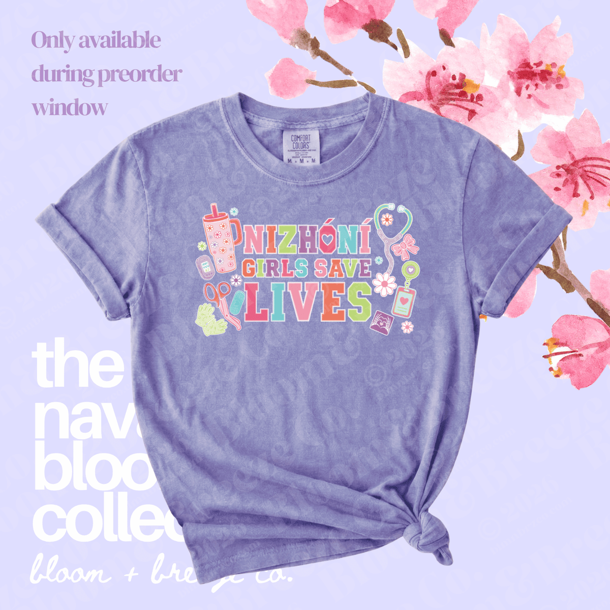 A lavender heathered graphic t-shirt with rolled sleeves and a knotted hem, featuring the text 'NIZHONI GIRLS SAVE LIVES' in colorful letters with medical-themed illustrations. The shirt is displayed on a light lavender background decorated with pink cherry blossoms and text overlays.