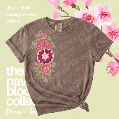A short-sleeve crewneck t-shirt in a washed, faded brown color, featuring a vertical graphic print of pink flowers and a central pink-and-white geometric pattern. The shirt is styled with a knot at the bottom hem against a light green background decorated with pink watercolor flowers and text overlays.