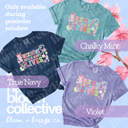 Three graphic T-shirts in different colors are displayed together on a light blue background with pink cherry blossom graphics. The shirts are labeled 'True Navy', 'Chalky Mint', and 'Violet'.