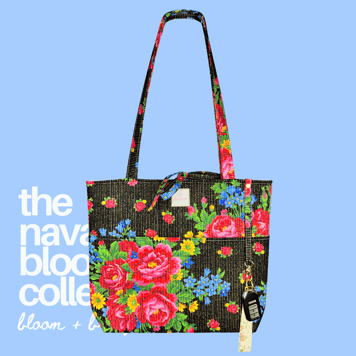 Black floral tote with vivid red, blue, and yellow flowers, long shoulder straps, and car keys clipped to the exterior.