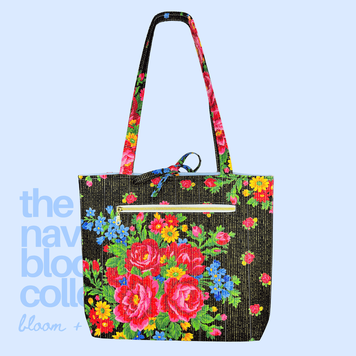 Back view of a black floral tote with vivid red, blue, and yellow flowers, long shoulder straps, and a gold-zippered exterior pocket.