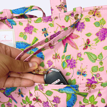 Close-up of a pink hummingbird, butterfly, and floral-print tote as a hand places car keys into the front pocket.
