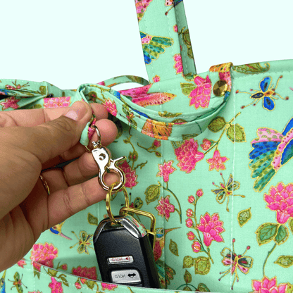 Close-up of a mint hummingbird, butterfly, and floral-print tote as a hand clips car keys to an exterior ring