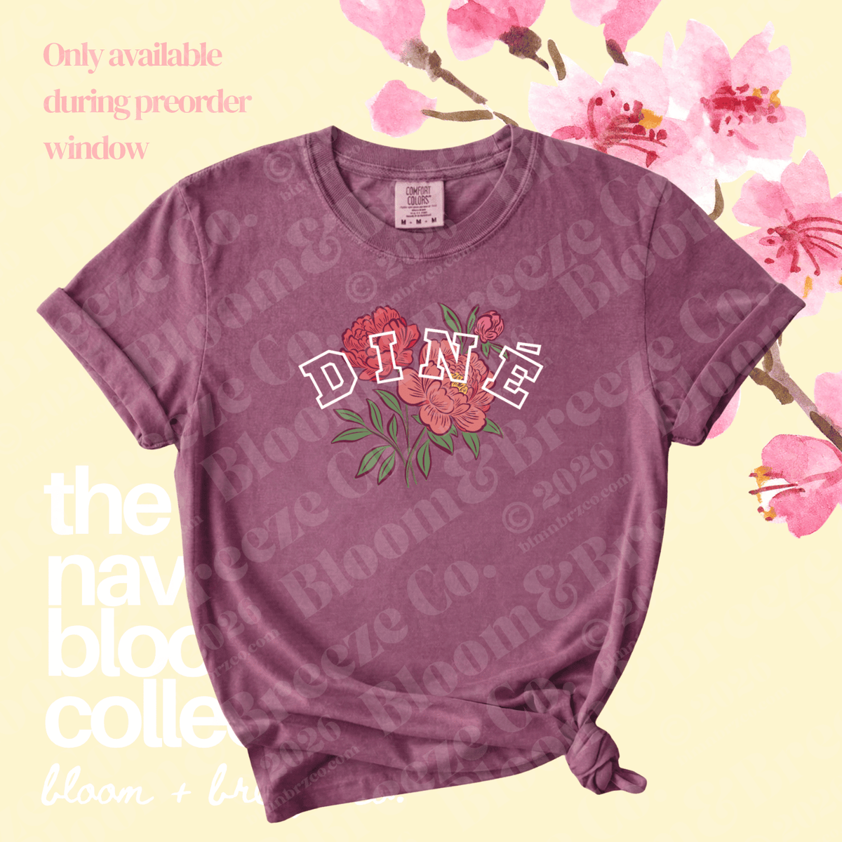 A mauve short-sleeve t-shirt with a 'DINÉ' graphic featuring red flowers and green leaves, styled with a knot at the bottom hem against a pale yellow background with pink cherry blossoms.
