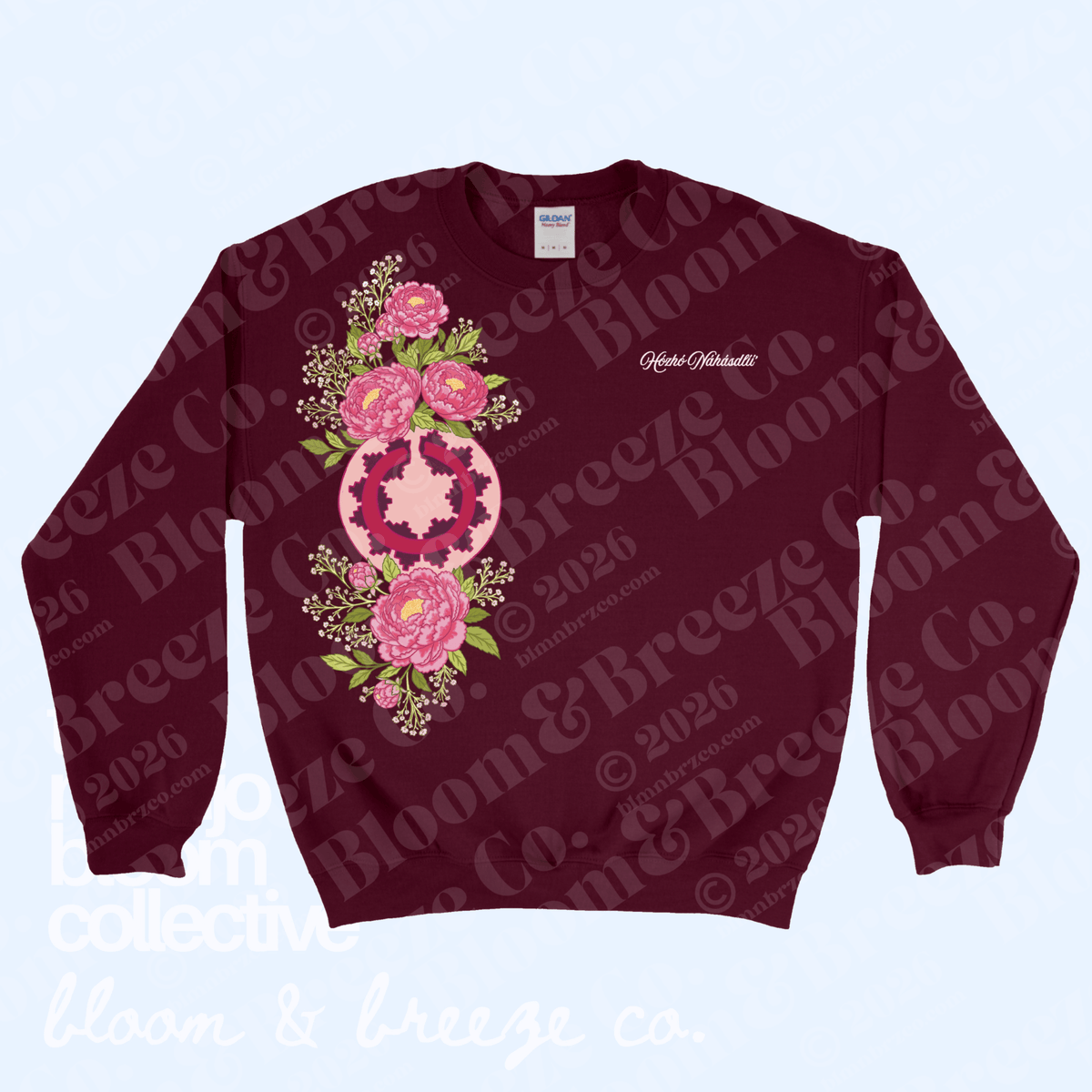 A crewneck sweatshirt in deep burgundy, featuring a large pink and green floral mandala graphic on the front and a small white script logo on the left chest. The sweatshirt is displayed flat against a light blue background with a repeating watermark pattern.