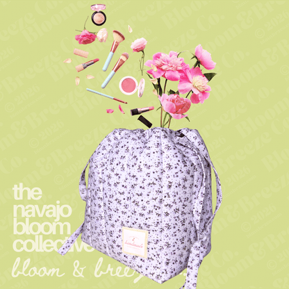 A drawstring cosmetic bag with a light purple and white floral print, shown with pink flowers and makeup items floating out of the top against a pale green background. Text on the left reads 'the navajo bloom collective bloom & bree'.