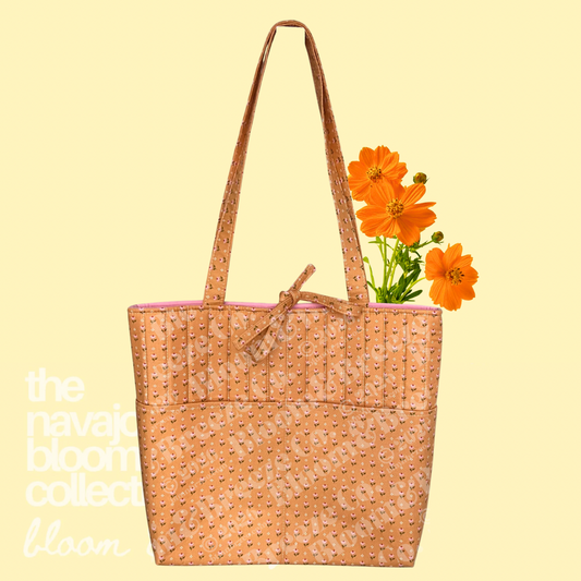 Yellow-orange floral quilted tote bag with long straps, front pockets, and orange flowers on a soft yellow background.