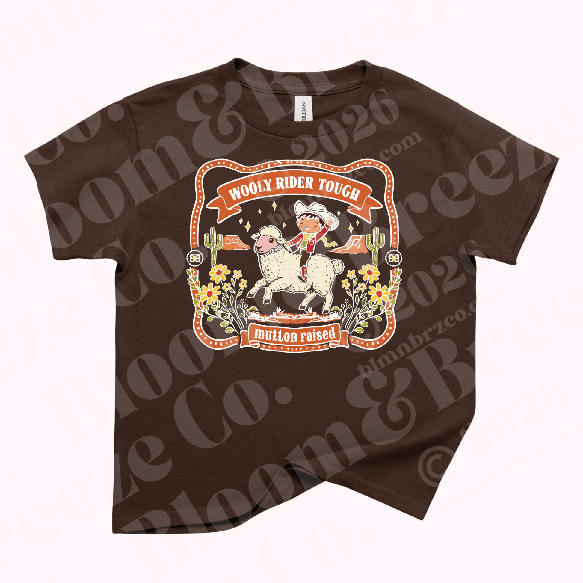 Brown youth t-shirt with vintage western style graphic of a child riding a sheep surrounded by desert flowers and cacti, reading “Wooly Rider Tough” and “mutton raised.”