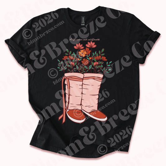 Black t-shirt with a graphic of pink navajo wrap moccasins and flowers blooming from moccasins on a white background