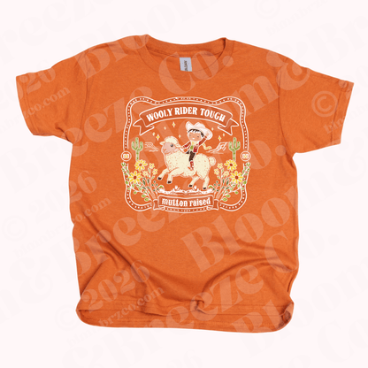 Orange t-shirt with a little cowboy riding bucking sheep and text reading wooly rider tough, mutton raised, buckle style graphic on a white background