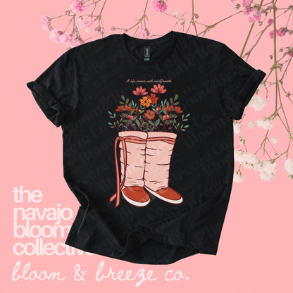 Black wildflower moccasin graphic tee on a soft pink floral background.