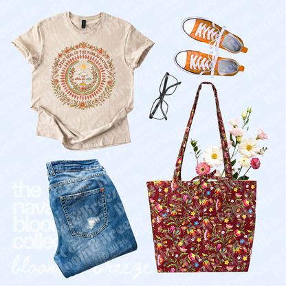 Cream Great Seal of the Navajo Nation graphic tee styled with jeans, orange sneakers, black glasses, and a burgundy floral quilted tote bag on a light blue background.