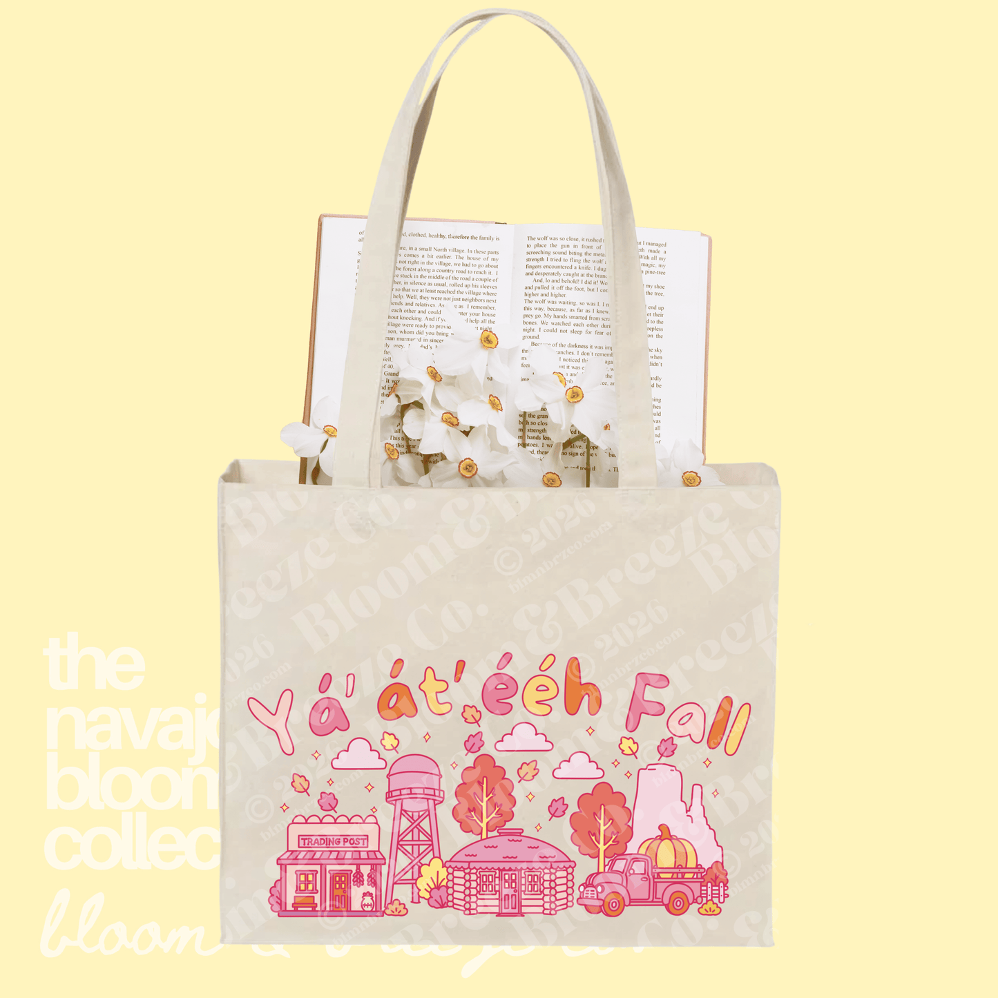 A cream canvas tote bag with white handles, featuring a colorful 'Yá átéeh Fall' illustration in pink and orange. The bag is shown filled with an open book and white flowers, set against a pale yellow background with a faint watermark.